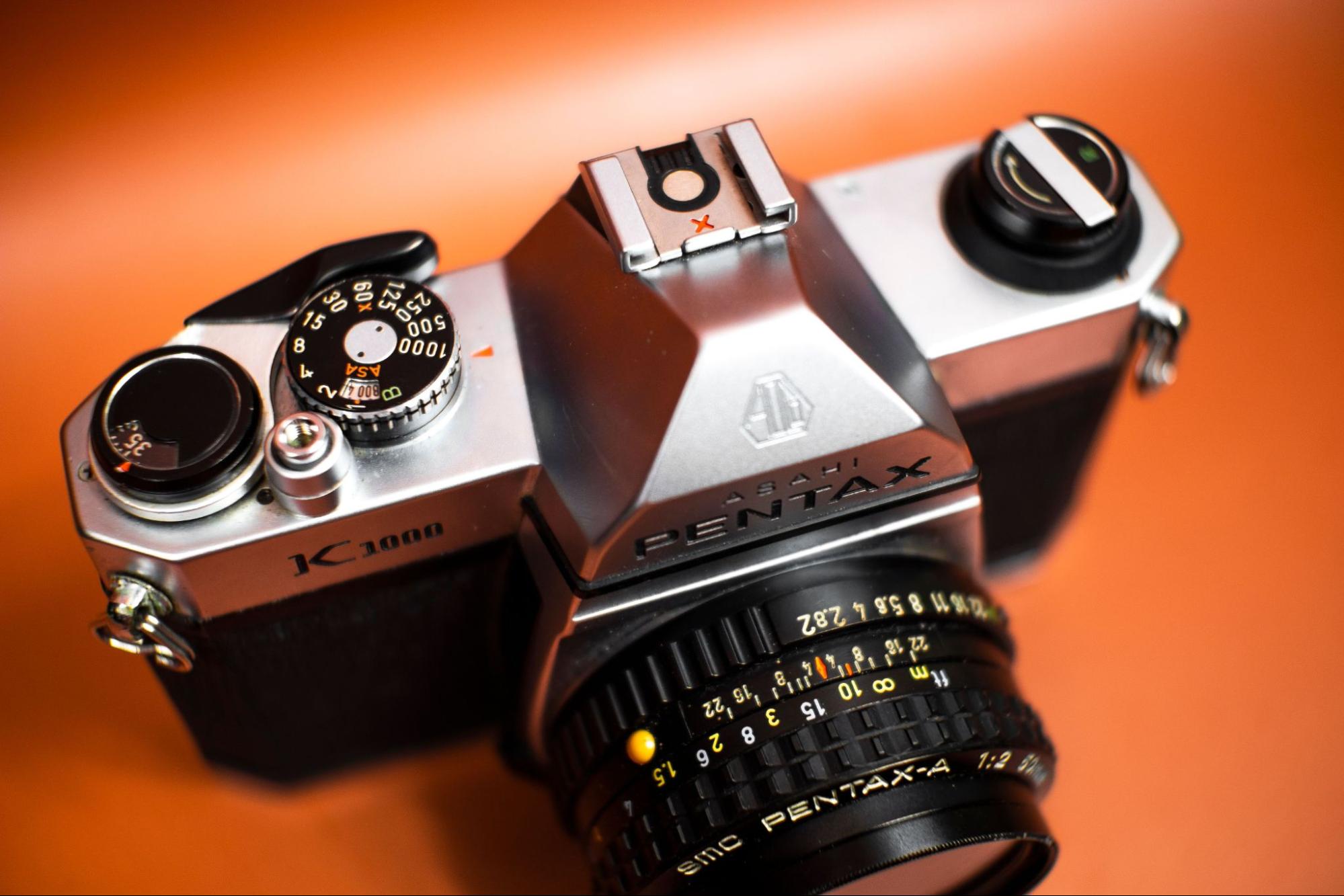 Pentax K1000 mechanical film camera showing its shutter speed dial and aperture ring