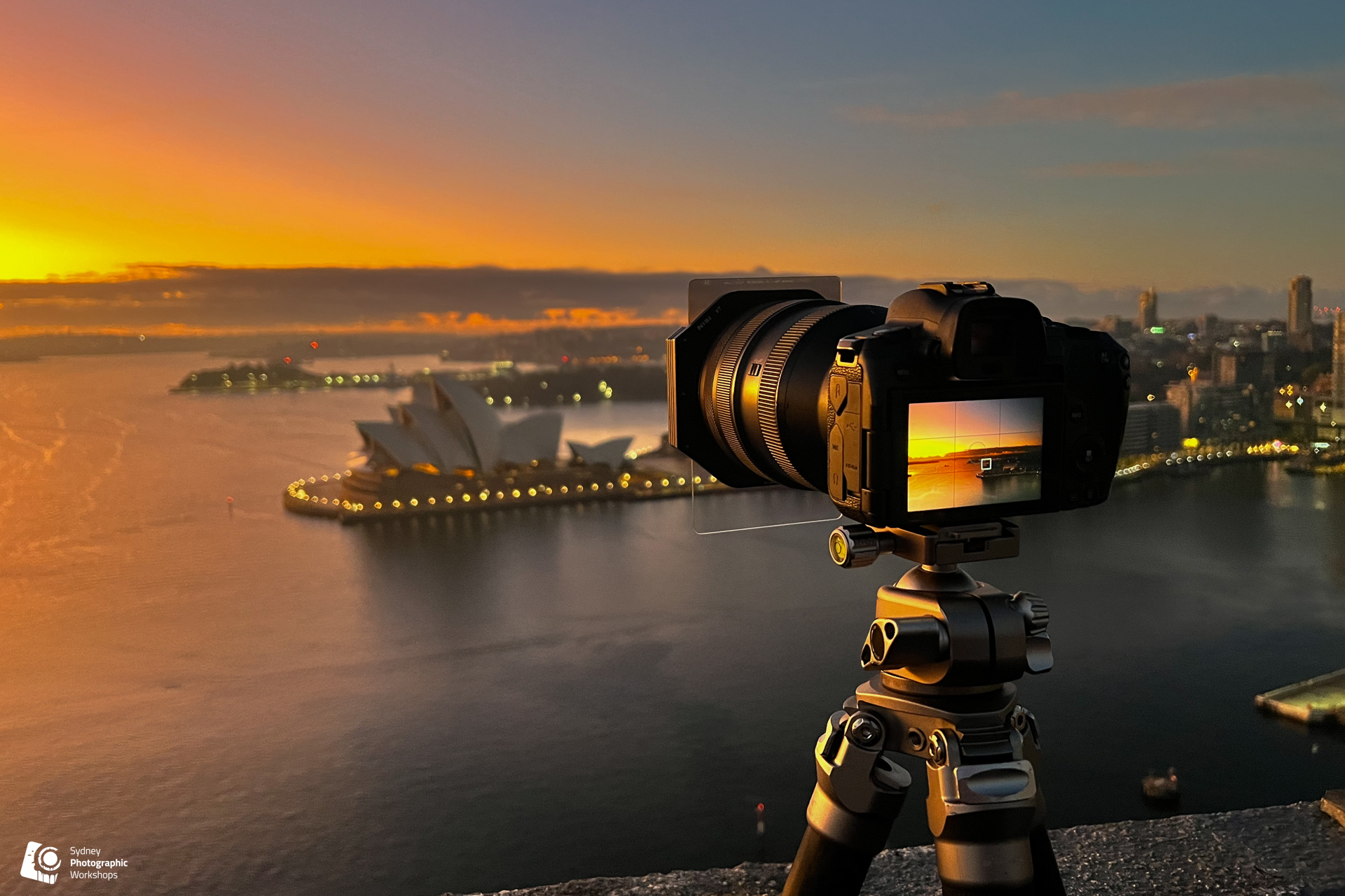 Camera on a tripod photographing Sydney Harbour and the Opera House at sunset
